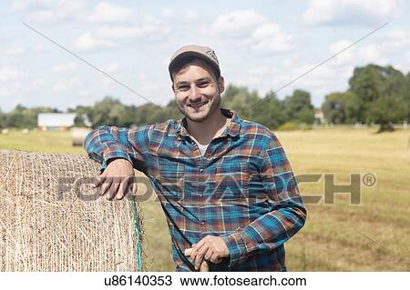 Farmer leaning against hay bale looking at camera smiling View Large Photo Image Stock Image - Farmer leaning against hay bale looking at camera smiling. Fotosearch