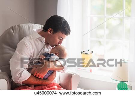 Picture - Father kissing baby son (0-1 months) by window. Fotosearch