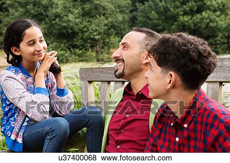 Stock Photo - Father sitting on bench with son and daughter, laughing. Fotosearch