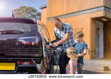 Stock Image - Father with children, charging electric car. Fotosearch