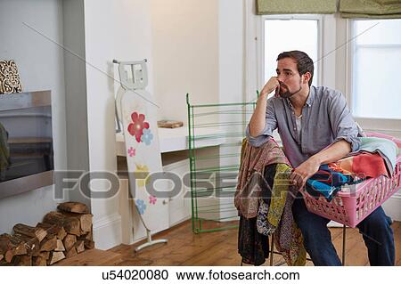 Stock Image - Fed up mid adult man with basket of laundry in living room. Fotosearch