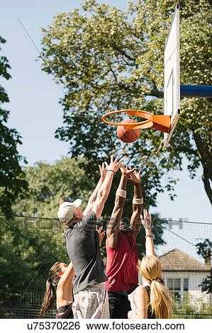 Stock Photograph - Female and male basketball players throwing ball at basketball hoop. Fotosearch