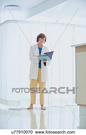 Female doctor reading medical notes at nurses station in hospital View Large Photo Image Stock Image - Female doctor reading medical notes at nurses station in hospital. Fotosearch