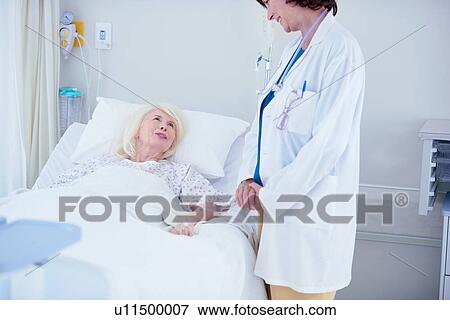 Stock Photo - Female doctor talking to senior female patient in hospital bed. Fotosearch