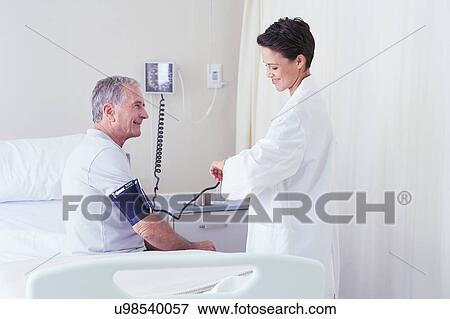 Female doctor using blood pressure gauge and timing pulse of senior male patient View Large Photo Image Stock Photo - Female doctor using blood pressure gauge and timing pulse of senior male patient. Fotosearch