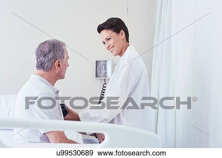 Stock Photo - Female doctor using blood pressure gauge on senior male patient on hospital bed. Fotosearch