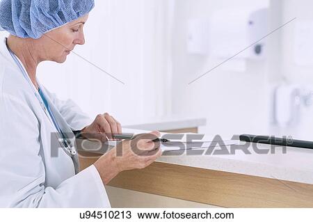 Stock Image - Female doctor writing medical notes at nurses station in hospital. Fotosearch
