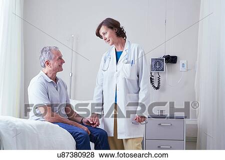 Stock Photo - Female doctors explaining to senior male patient on hospital bed. Fotosearch