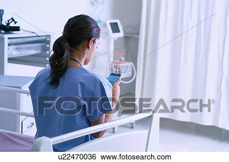 Stock Photograph - Female medic sitting on hospital bed reading smartphone texts. Fotosearch