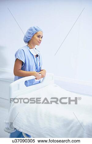 Stock Photography - Female nurse standing by hospital bed. Fotosearch