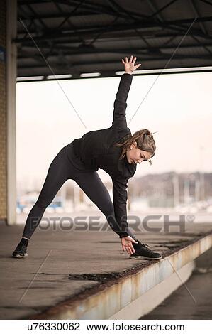 Stock Image - Female runner bending forward stretching on warehouse platform. Fotosearch