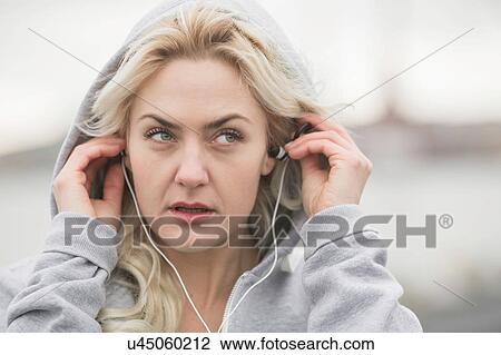 Stock Image - Female runner putting in earphones on dockside. Fotosearch