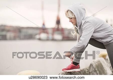 Stock Image - Female runner tying trainer laces on dockside. Fotosearch