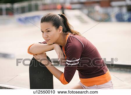 Stock Image - Female skateboarder in skatepark leaning on skateboard. Fotosearch