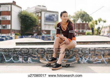 Stock Photo - Female skateboarder sitting in skatepark. Fotosearch