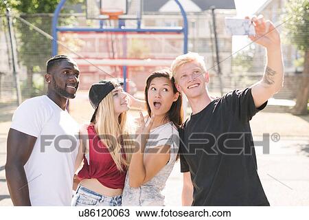 Four adult friends posing for smartphone selfie on basketball court View Large Photo Image Stock Image - Four adult friends posing for smartphone selfie on basketball court. Fotosearch