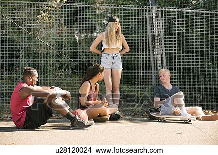 Picture - Four adult skateboarder friends sitting chatting on basketball court. Fotosearch
