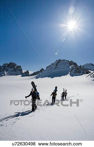 Stock Photo - Four male snowboarders hiking across snow-covered landscape, Trient, Swiss Alps, Switzerland. Fotosearch