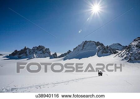 Stock Photograph - Four male snowboarders hiking across snow-covered landscape, Trient, Swiss Alps, Switzerland. Fotosearch