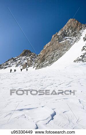 Stock Photo - Four male snowboarders hiking up snow-covered landscape, Trient, Swiss Alps, Switzerland. Fotosearch