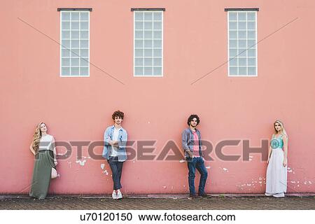 Stock Image - Friends standing against pink wall background. Fotosearch