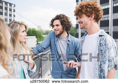 Stock Image - Friends standing and chatting beside rail. Fotosearch