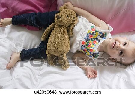 Girl (18-23 months) lying on bed with teddy bear View Large Photo Image Stock Photo - Girl (18-23 months) lying on bed with teddy bear. Fotosearch