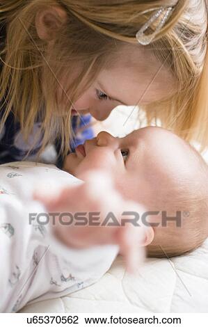 Stock Image - Girl (2-3) face to face with baby brother (6-11 months). Fotosearch