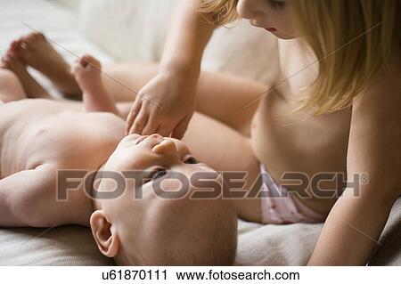 Stock Image - Girl (2-3) looking at baby brother (6-11 months) on bed. Fotosearch
