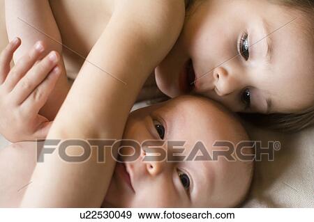 Stock Photo - Girl (2-3) lying on bed with baby brother (6-11 months). Fotosearch
