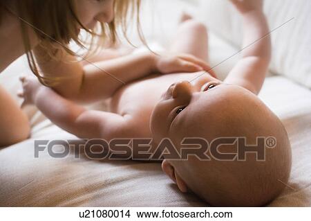 Girl (2-3) touching baby brother (6-11 months) lying on bed View Large Photo Image Picture - Girl (2-3) touching baby brother (6-11 months) lying on bed. Fotosearch
