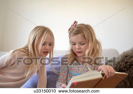 Girl and her sister reading in living room View Large Photo Image Stock Image - Girl and her sister reading in living room. Fotosearch