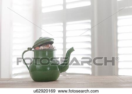 Stock Photo - Green vintage teapot full of British coins on table. Fotosearch