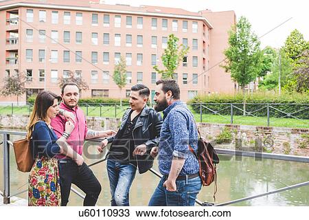 Stock Image - Group of friends chatting by river. Fotosearch