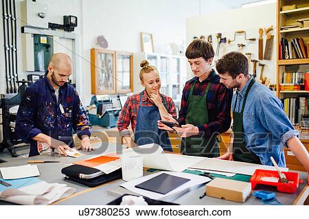 Stock Image - Group of young craftspeople using digital tablet in book arts workshop. Fotosearch