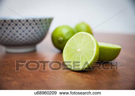Stock Photo - Halved and whole limes on wooden table. Fotosearch