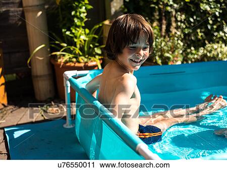 Stock Image - Happy boy playing in inflatable pool on summer day. Fotosearch