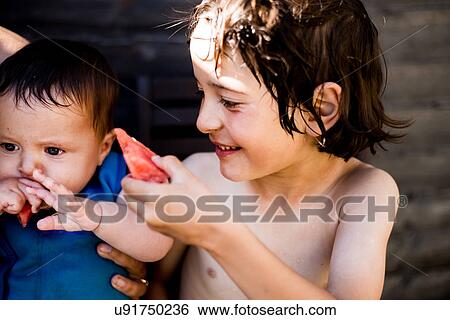 Stock Photograph - Happy brothers eating watermelon on summer day. Fotosearch