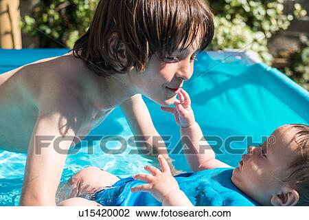 Stock Image - Happy brothers playing in inflatable pool on summer day. Fotosearch