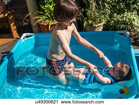 Stock Image - Happy brothers playing in inflatable pool on summer day. Fotosearch