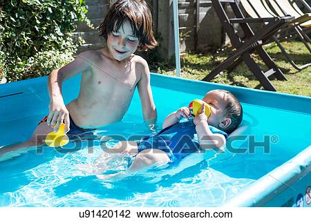 Stock Image - Happy brothers playing in inflatable pool on summer day. Fotosearch