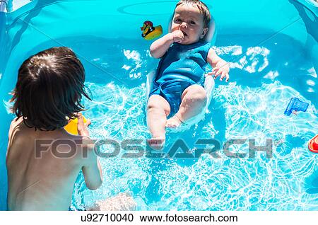 Stock Image - Happy brothers playing in inflatable pool on summer day. Fotosearch