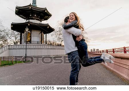 Stock Photography - Happy young man hugging girlfriend in Battersea Park, London, UK. Fotosearch