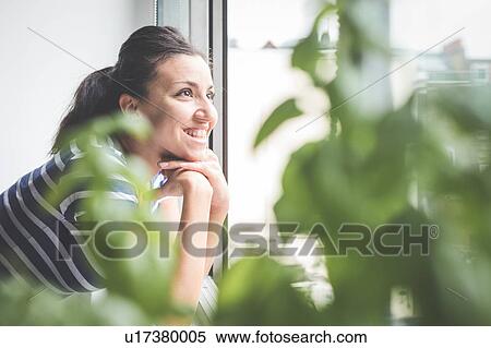 Stock Photography - Happy young woman looking through apartment window. Fotosearch