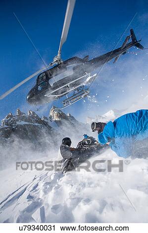 Stock Image - Helicopter leaving male snowboarders on mountain, Trient, Swiss Alps, Switzerland. Fotosearch