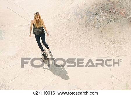 Stock Photograph - High angle of young female skateboarder skateboarding in skatepark. Fotosearch