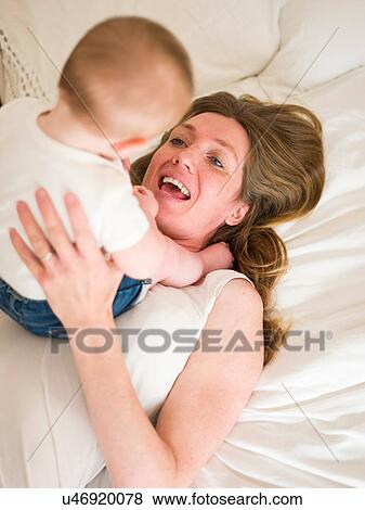 Stock Photo - High angle view of baby girl sitting on mother. Fotosearch