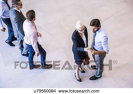 High angle view of two businessman and woman reading smartphone text in office atrium View Large Photo Image Picture - High angle view of two businessman and woman reading smartphone text in office atrium. Fotosearch