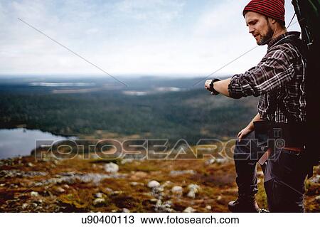 Stock Image - Hiker checking time on cliff top, Keimiotunturi, Lapland, Finland. Fotosearch