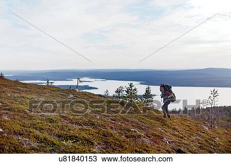 Stock Image - Hiker crossing field by lake, Keimiotunturi, Lapland, Finland. Fotosearch